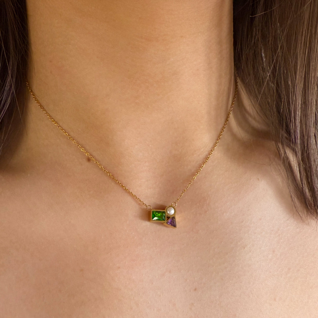 Necklace with green gemstone and pearl pendant on a person's neck