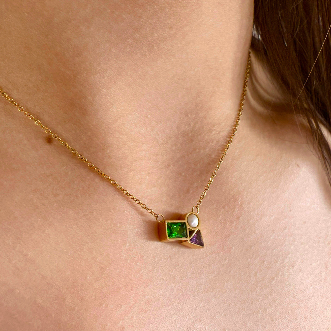 Gold necklace with a green gemstone worn by a person