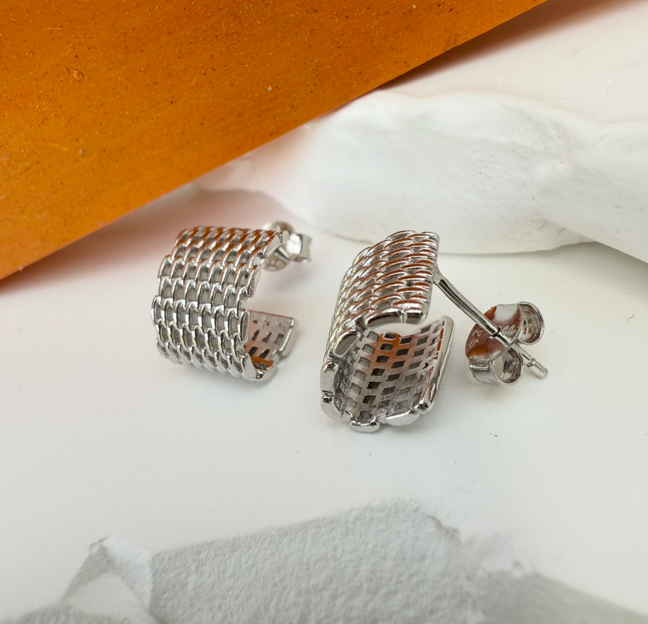 Silver hoop earrings on a white surface with an orange background