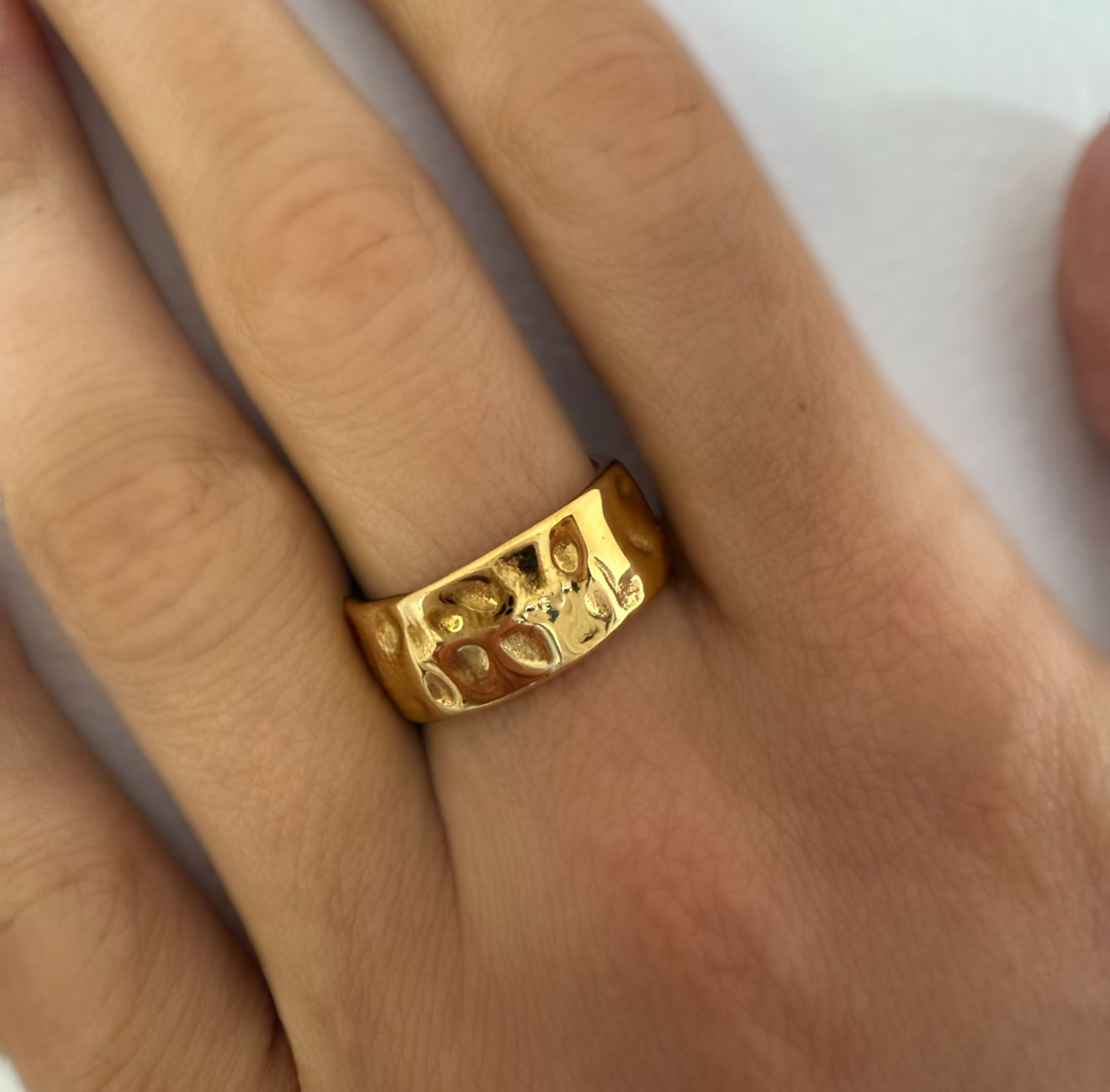 Gold ring with a textured design on a person's finger against a neutral background
