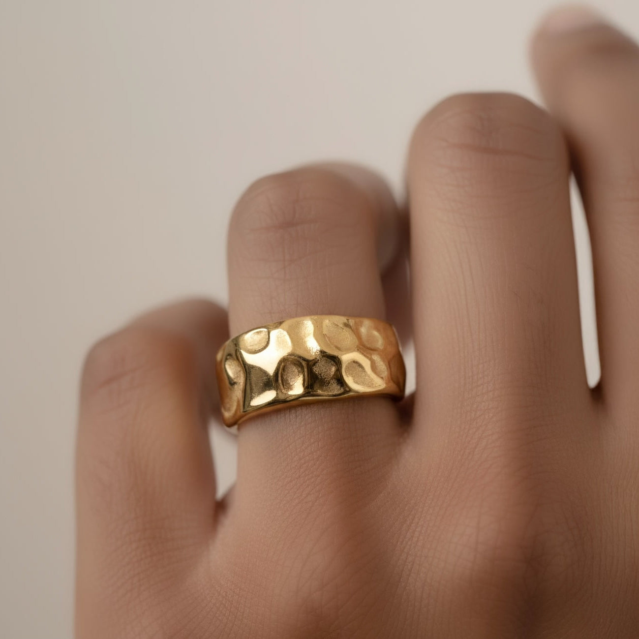 Gold ring on a finger against a neutral background