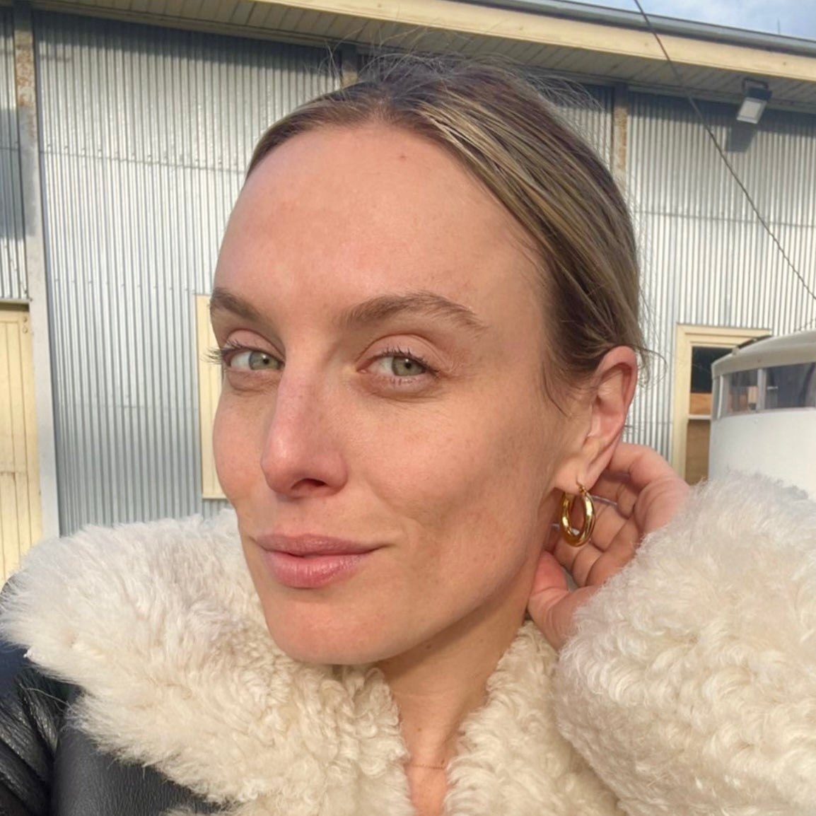 Woman wearing Hustle Hoops a white fur-lined coat with a building in the background