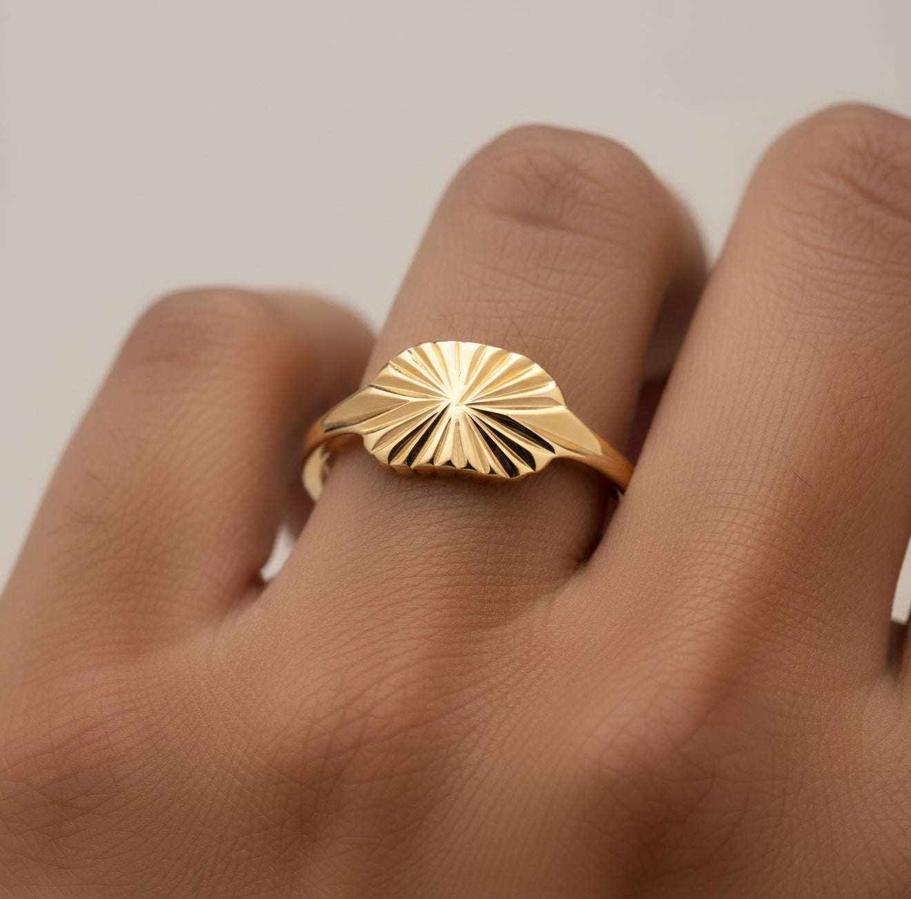 Gold ring with sunburst design on a finger against a neutral background