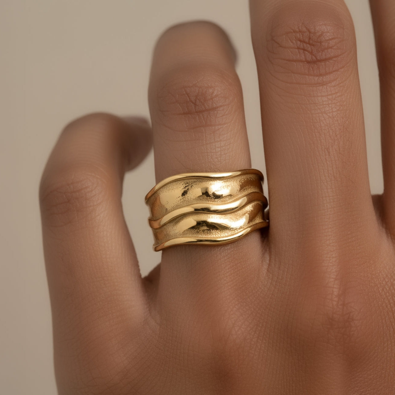 Gold band textured ring on a finger against a neutral background
