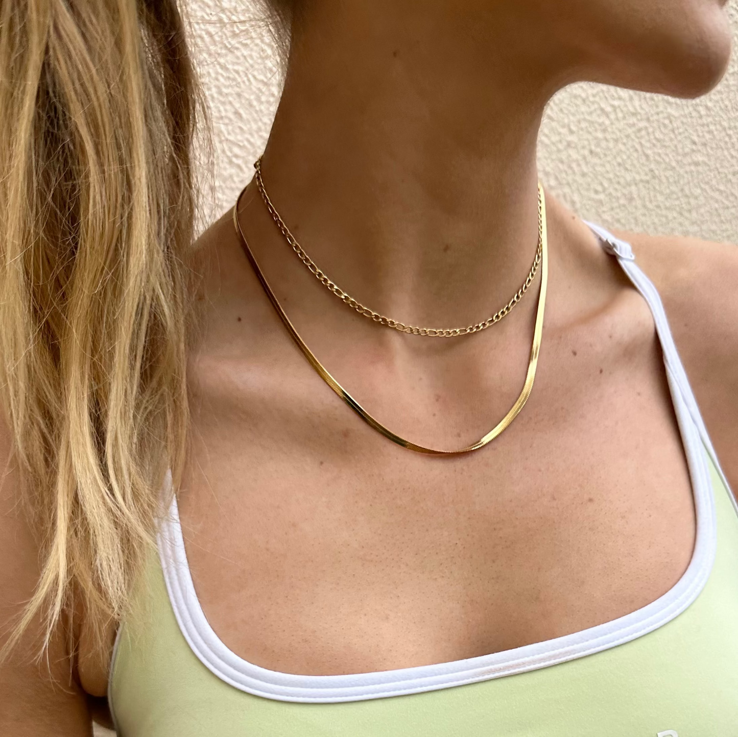 Close-up of a person wearing a Drop Shot and Sidewalk gold necklaces with a neutral background