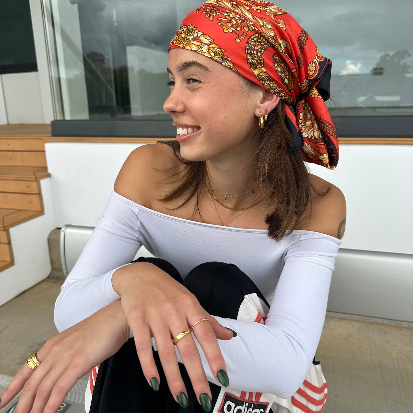 Woman seated casually outdoors wearing the Medley Ring paired with matching gold hoops and a printed headscarf.