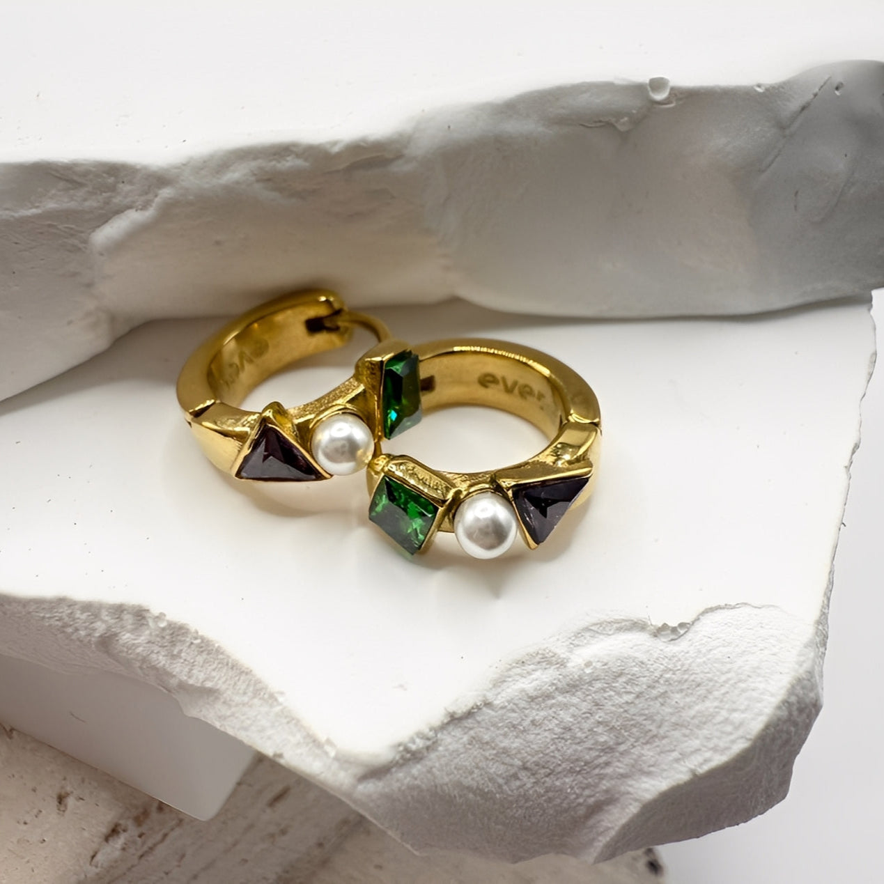 Gold hoop earrings with gemstones and pearls on a white stone surface