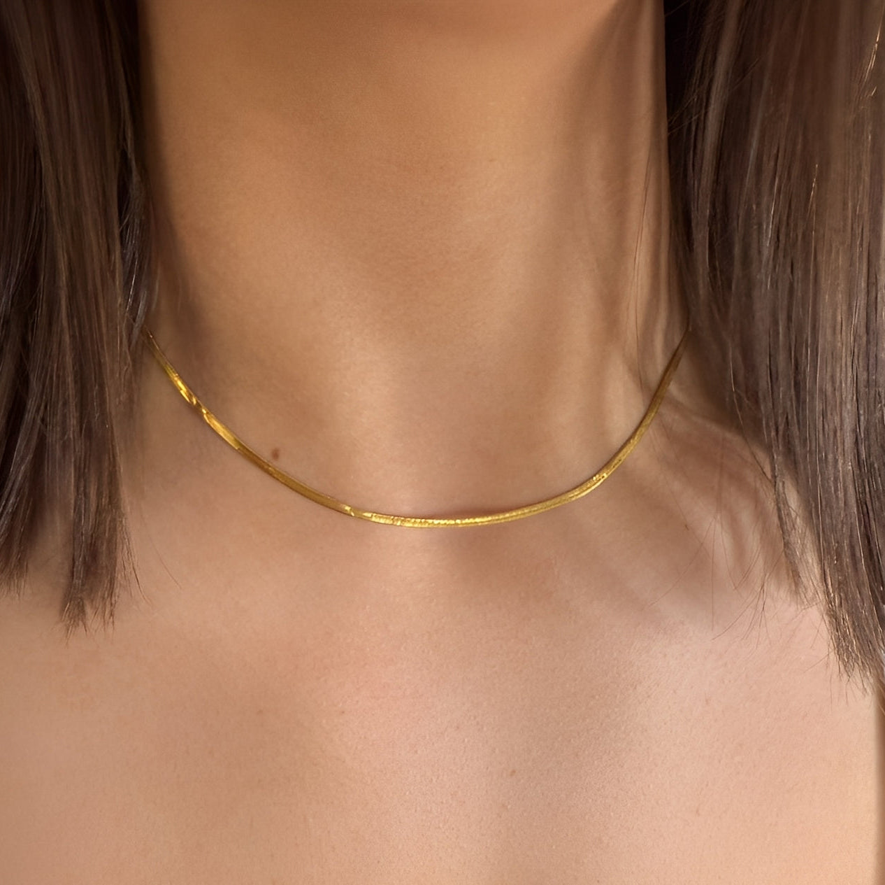 Gold necklace on a person with a neutral background