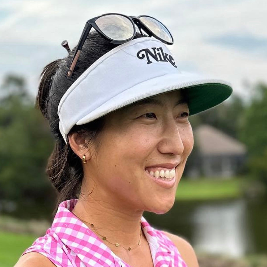 Woman wearing a white Nike visor with sunglasses on top, outdoors with Trackside Gold Huggies