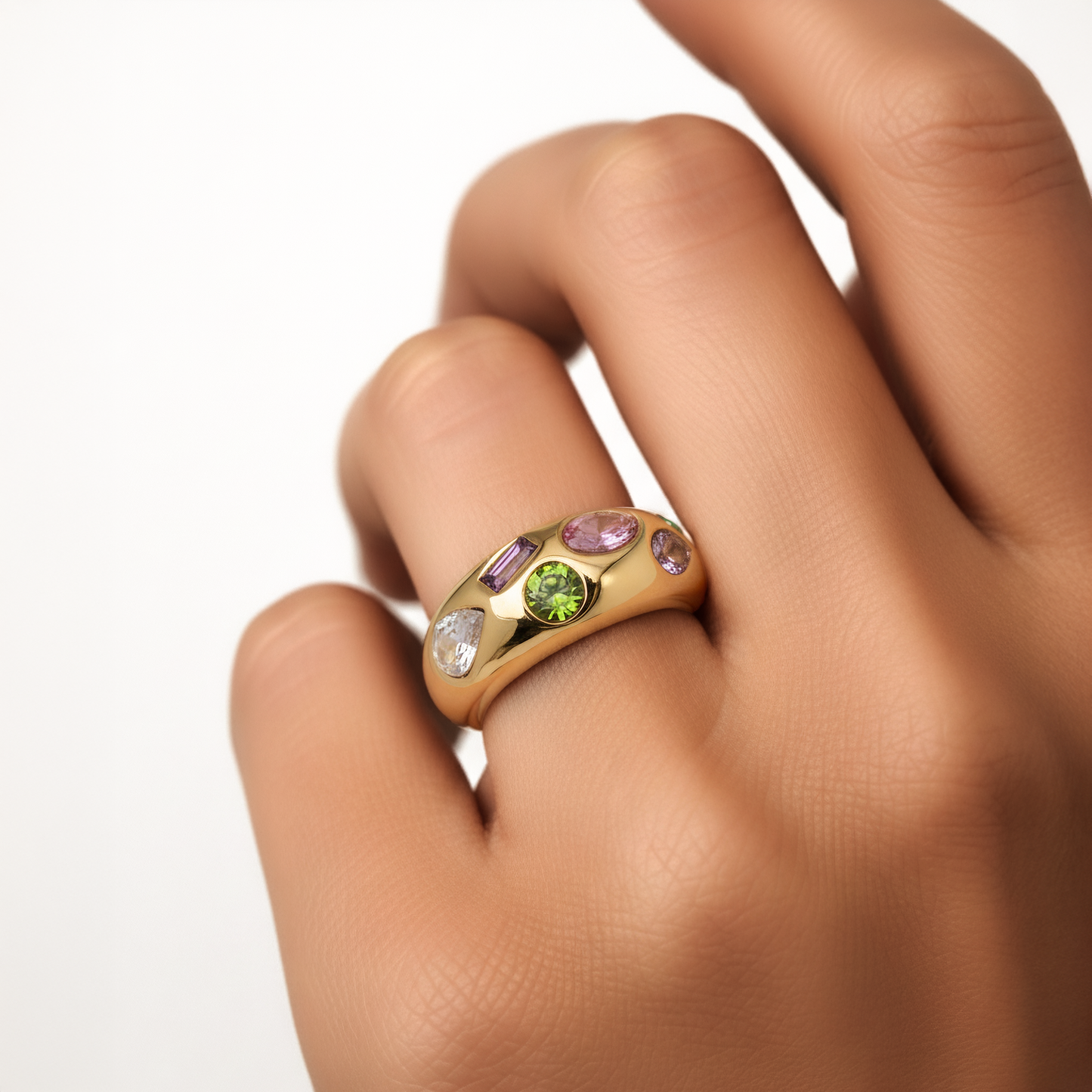 Gold ring with colorful gemstones on a hand against a white background