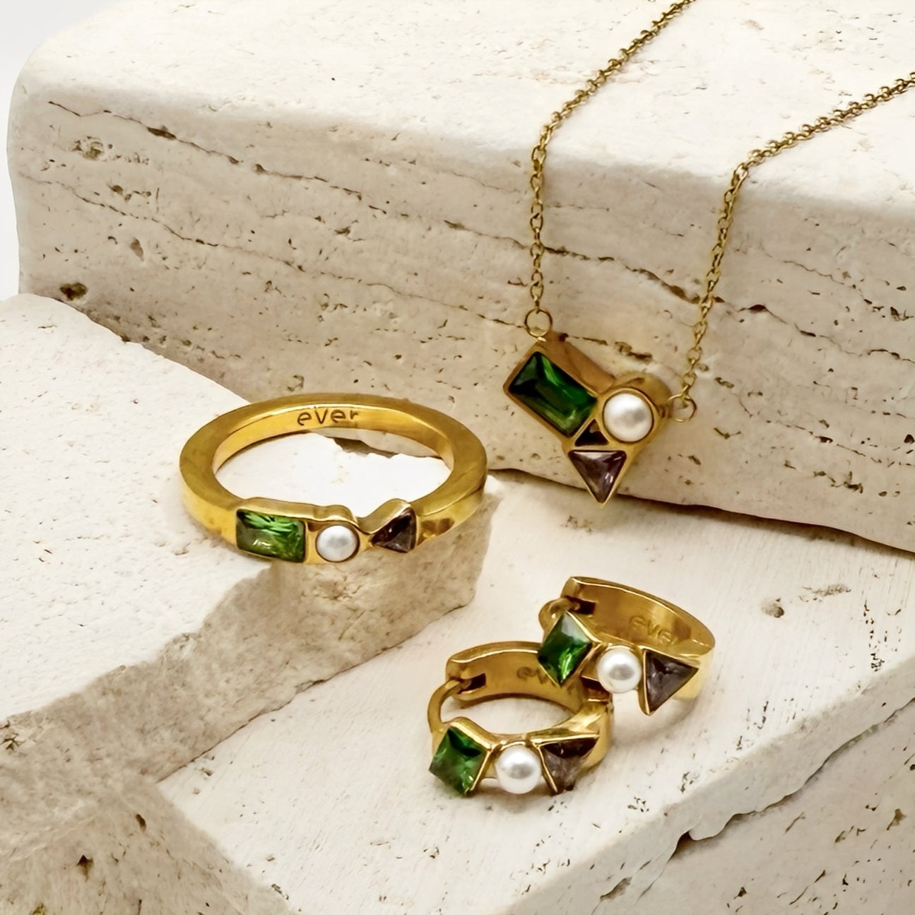 Gold jewelry set with rings and a necklace on a textured stone surface