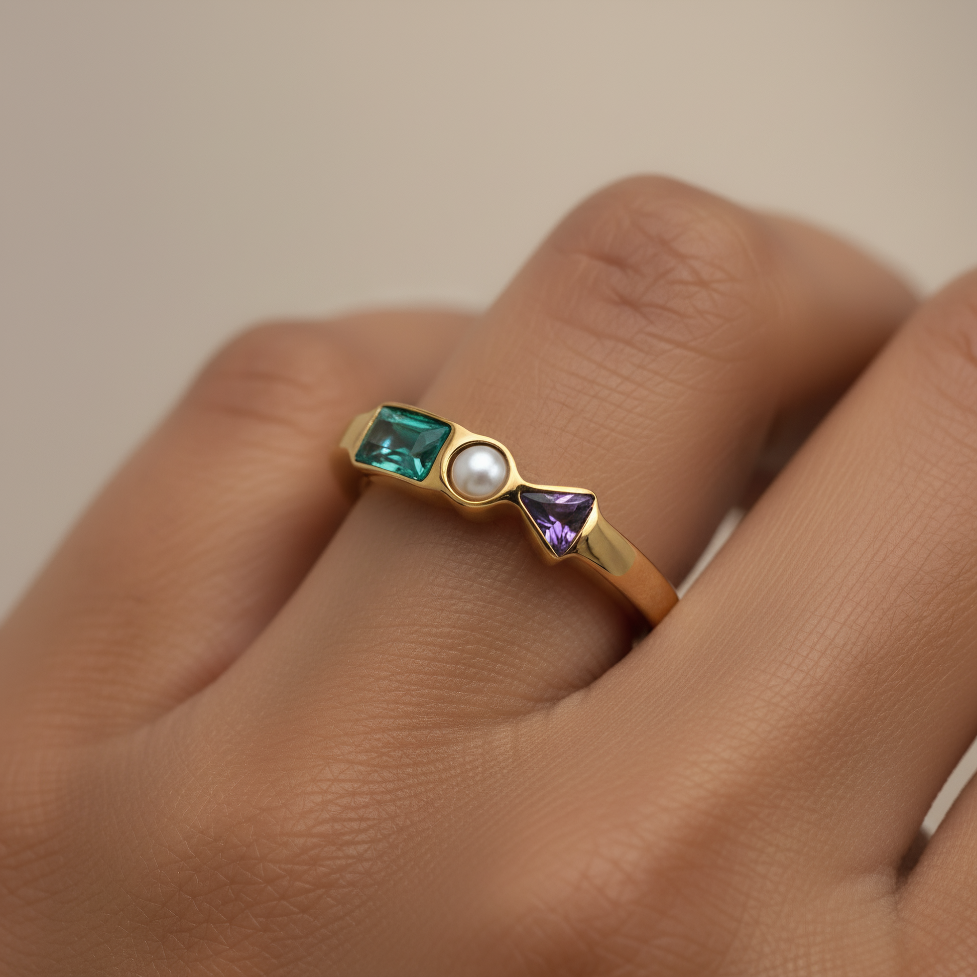 Gold ring with gemstones on a hand against a neutral background