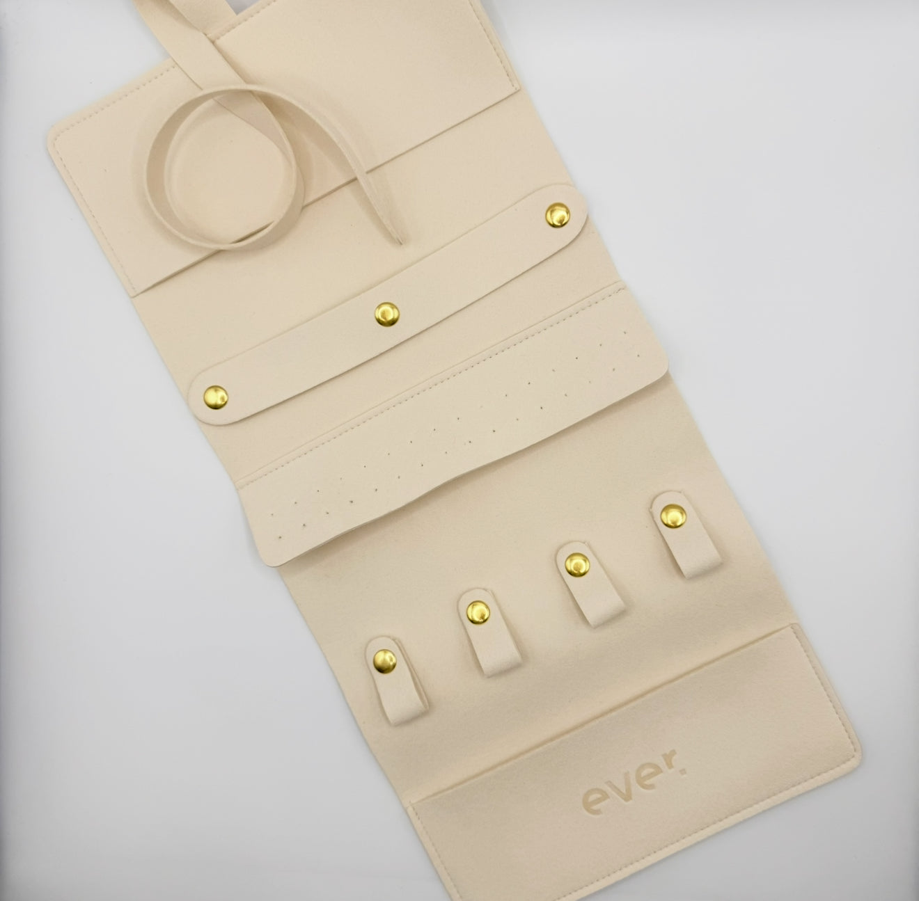 Beige jewelry roll-up organizer with gold accents on a light gray background