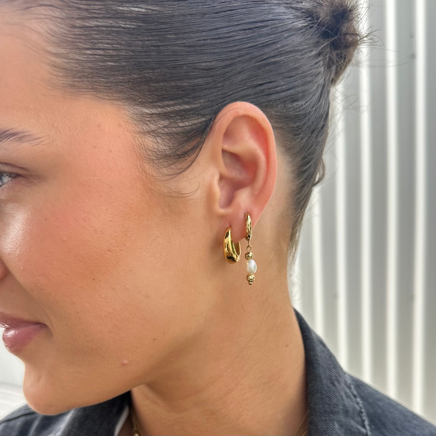 Close-up of a woman wearing gold Midnight Run Pearl Hoop earrings with pearl-like beads and layered with hoop earring.