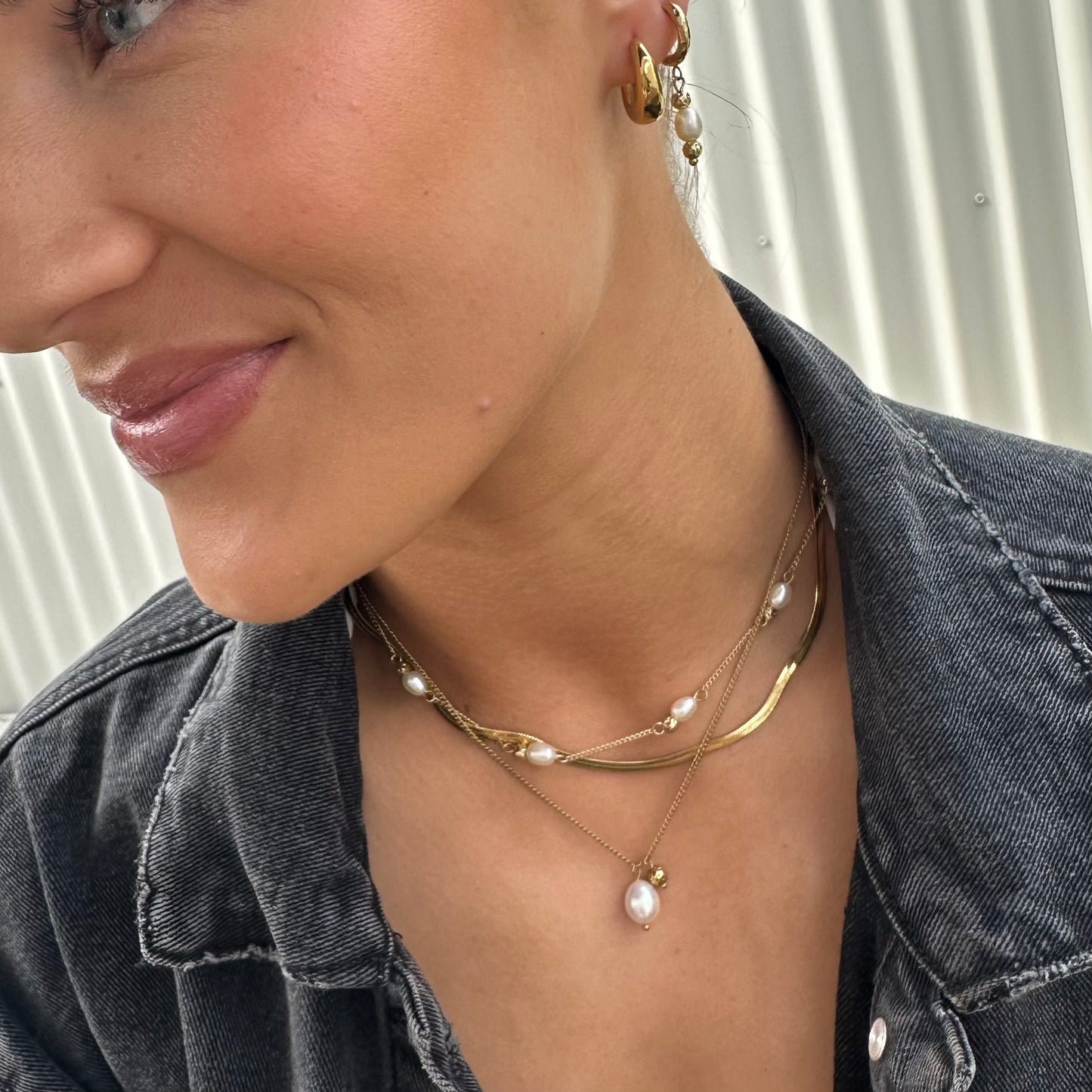 Close-up of a person wearing gold necklaces and earrings against a neutral background