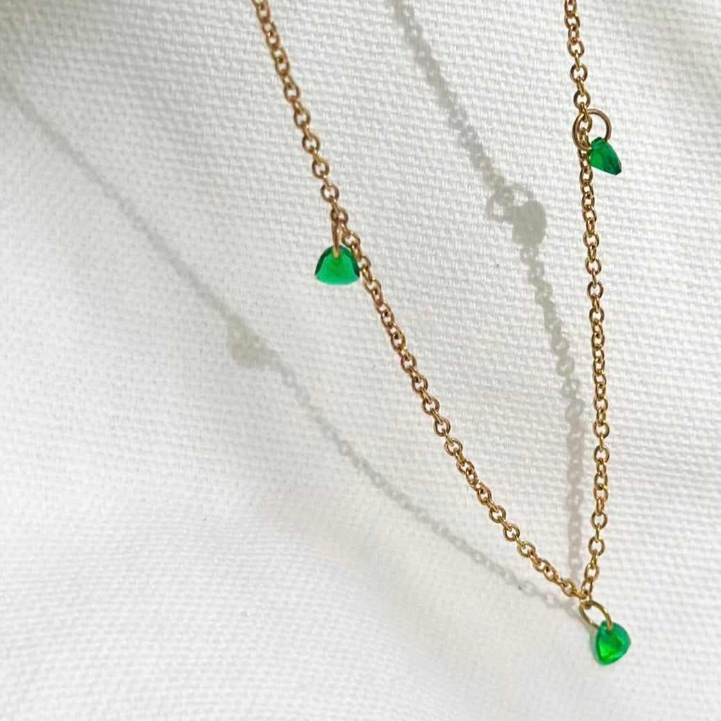 Close-up of Luxe Emerald Drop Necklace on fabric – gold chain with green gem drops, anti-tarnish and hypoallergenic