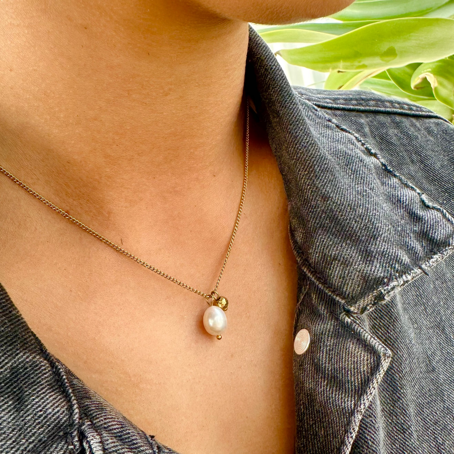 Person wearing the Off Court Pearl Necklace, gold necklace with a pearl pendant, standing outdoors with greenery in the background.