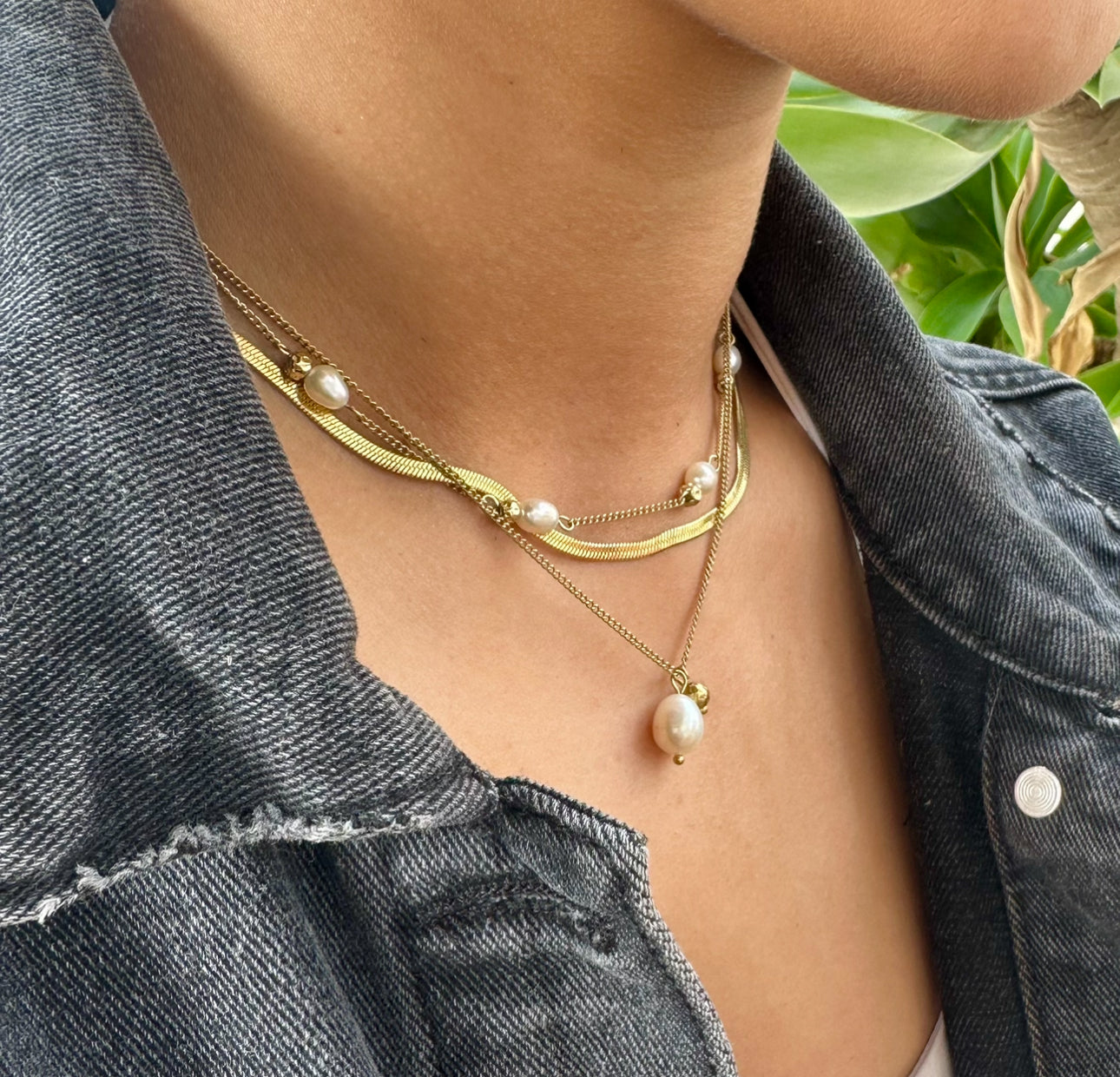 Person wearing a gold necklace with pearl beads against a denim jacket background