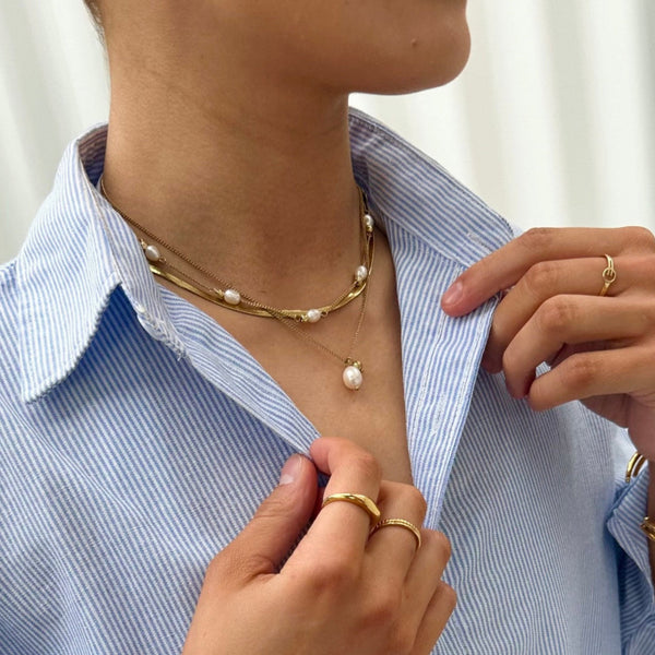 Person wearing a pearl necklace and gold jewelry on a light background