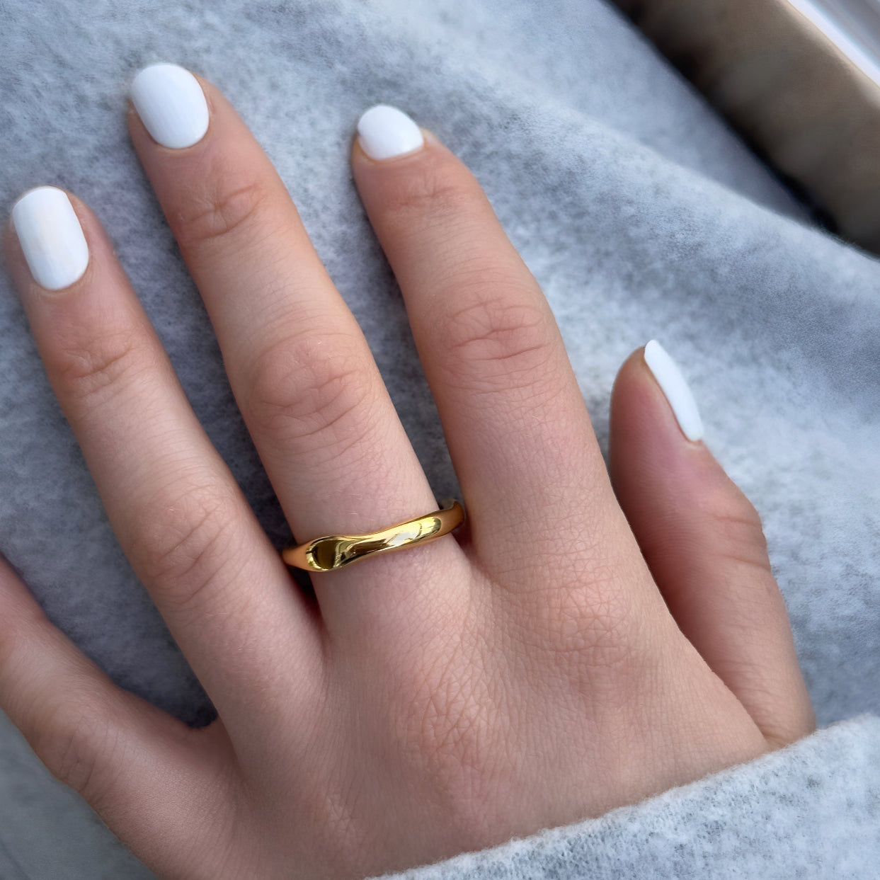 Gold ring on a hand with white nail polish against a gray background
