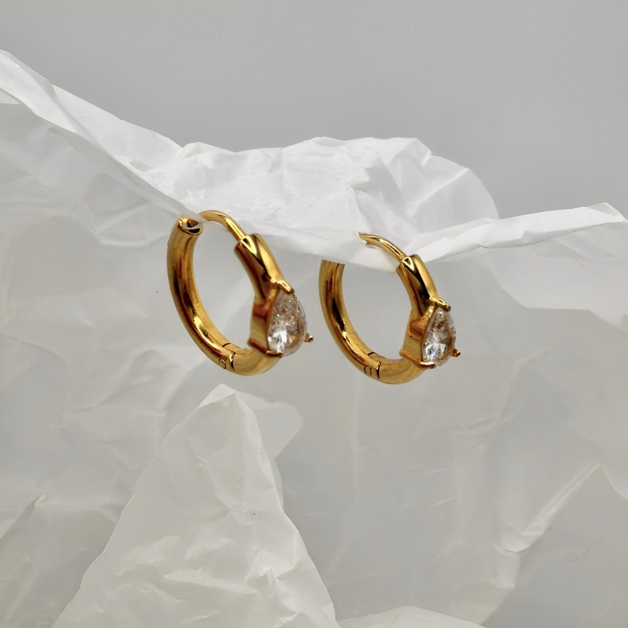 Gold hoop earrings with pear-shaped gemstones on a white fabric background
