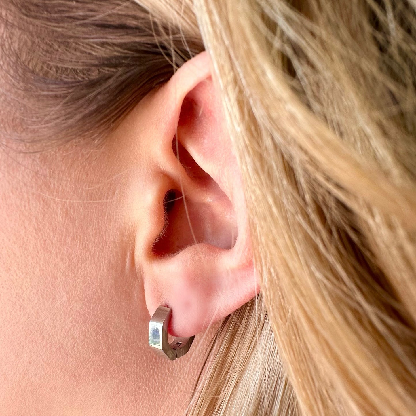 Close-up of a woman's ear wearing EVER Jewellery Silver Momentum Huggies, showing the sleek, polished design against blonde hair.