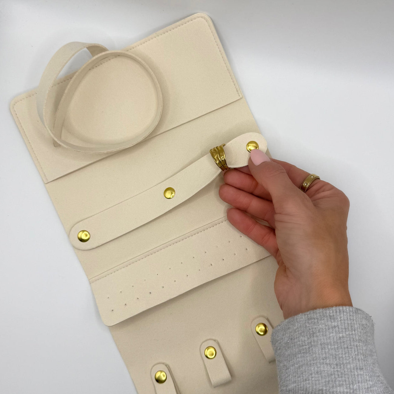 Beige leather bag with gold accents being adjusted by a hand on a light gray background
