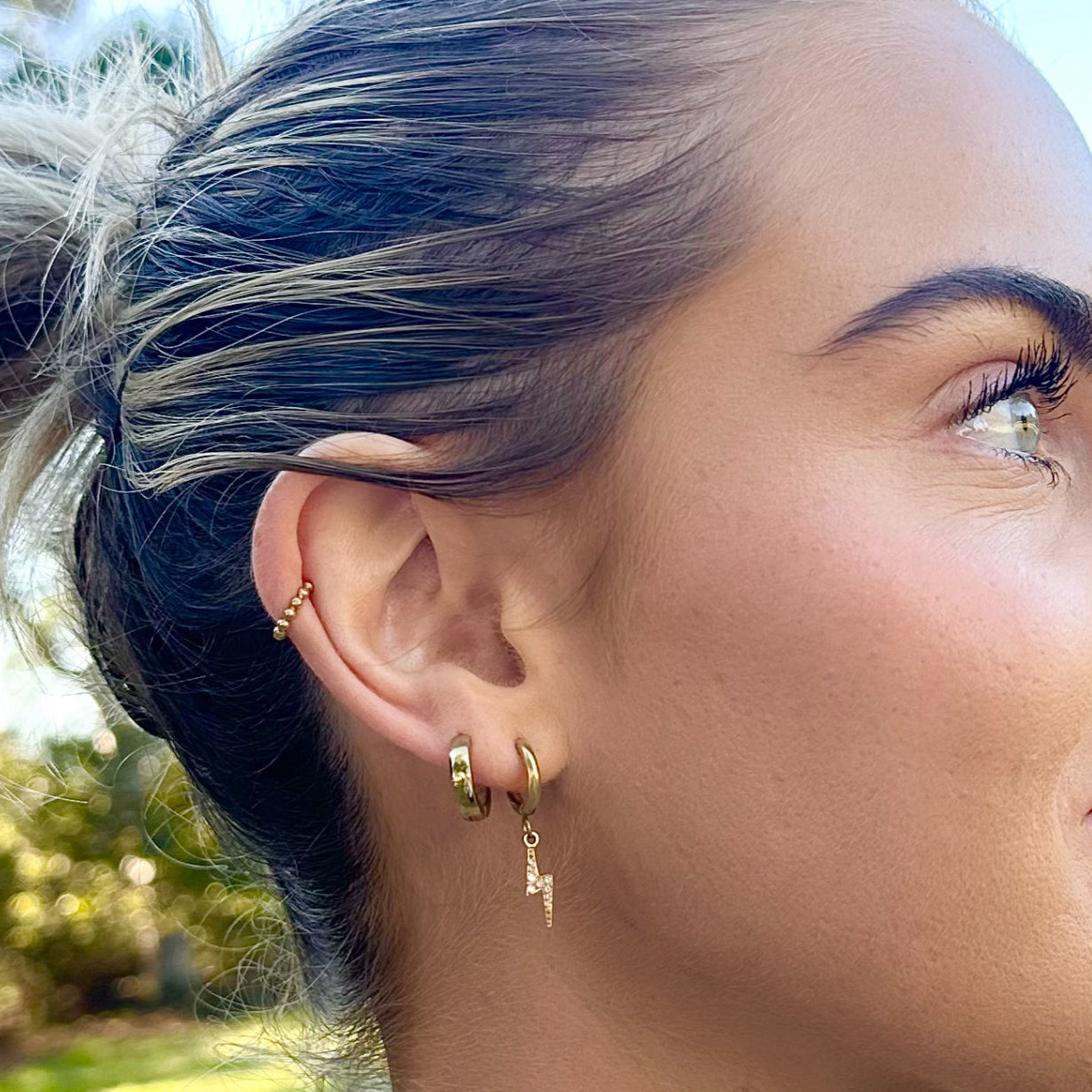 Close-up of a person wearing gold hoop earrings with a blurred outdoor background