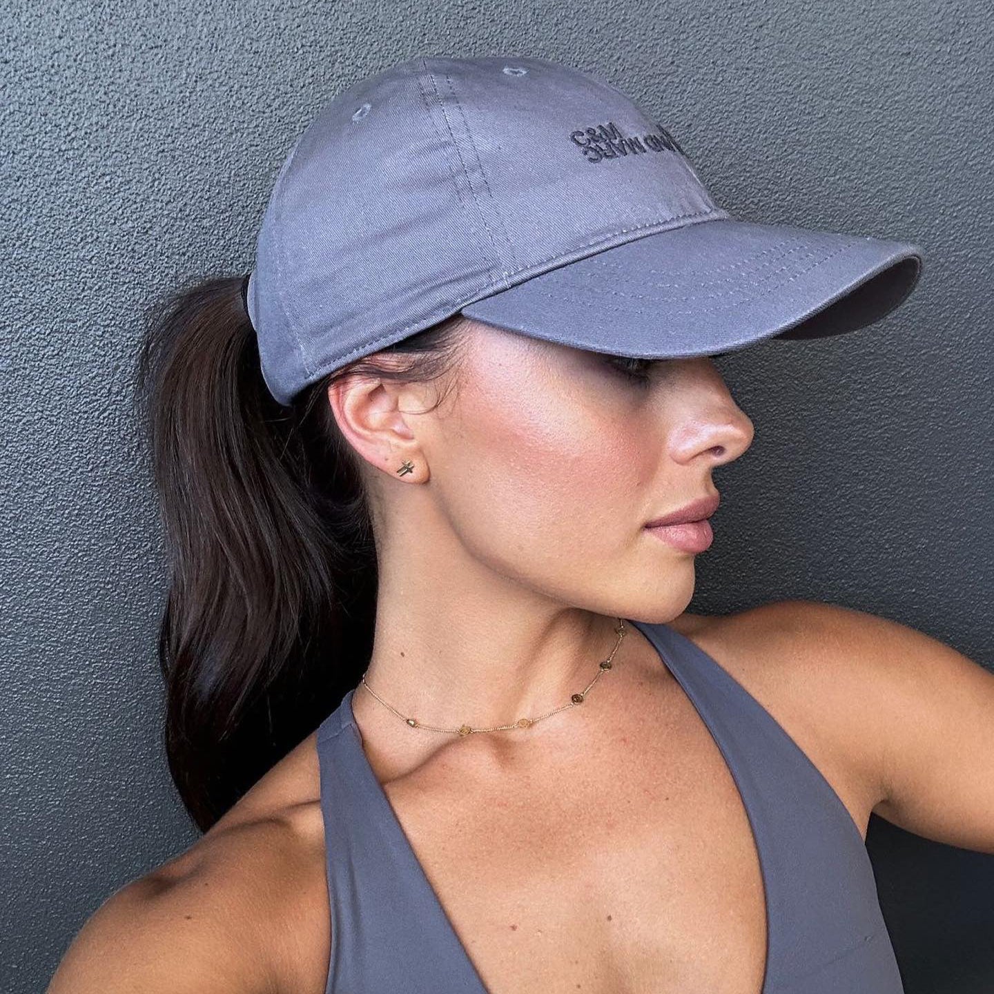 Woman wearing a grey sports bra and cap against a grey wall