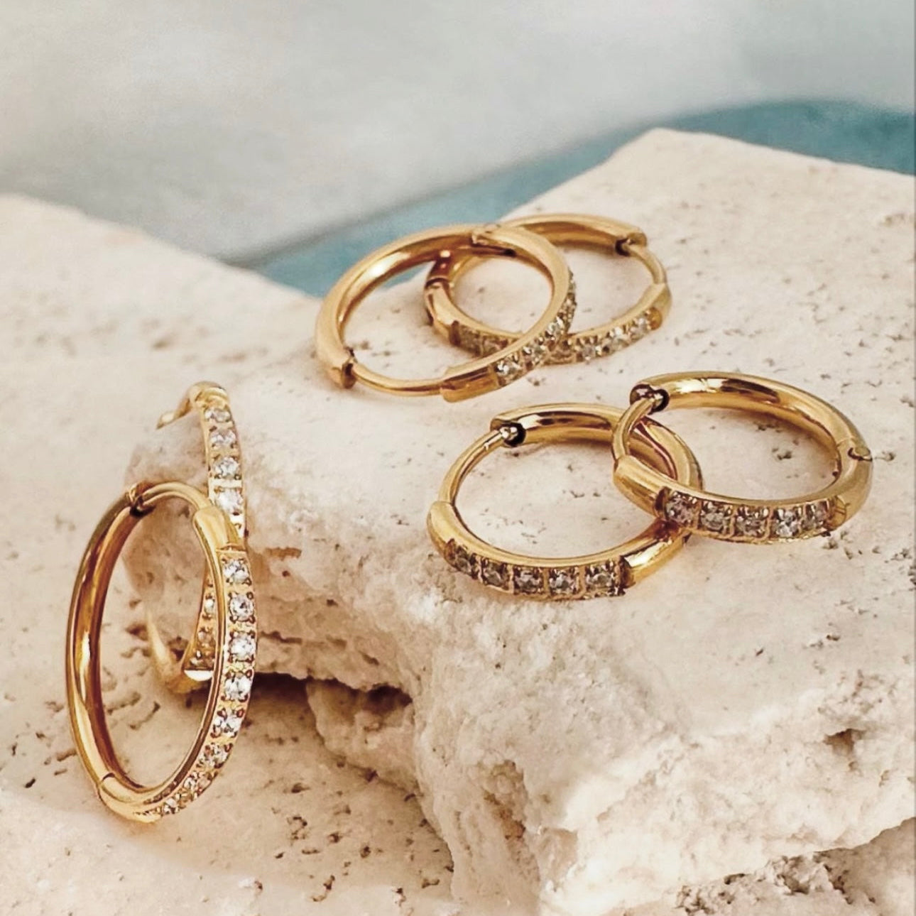 Gold hoop earrings with embedded stones on a textured surface