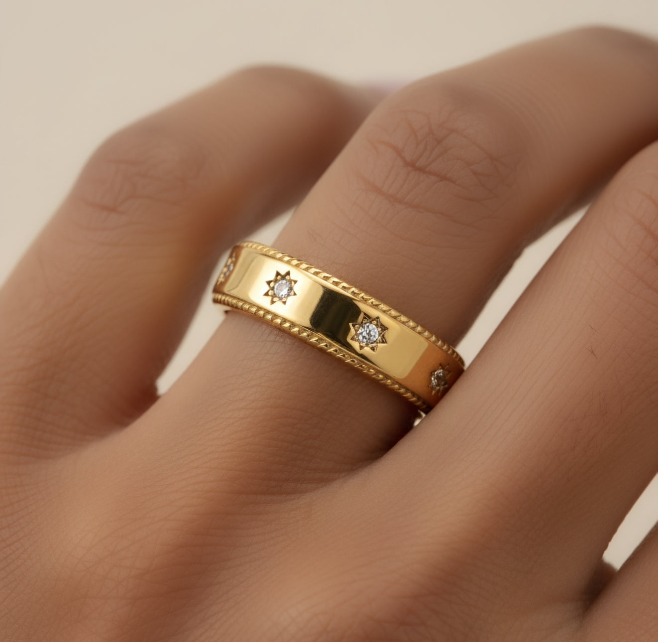 Gold ring with embedded diamonds on a finger against a neutral background