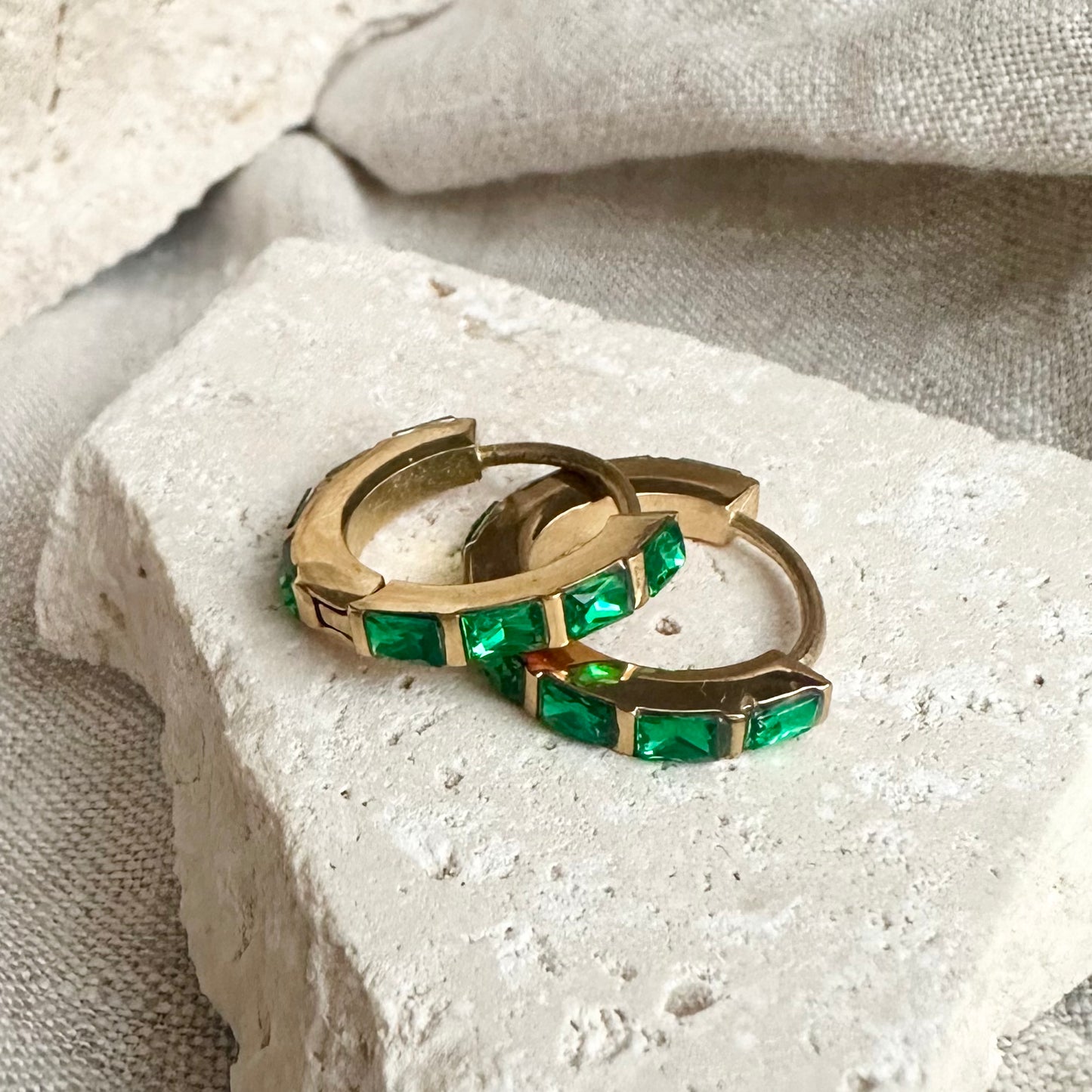 Gold hoop earrings with green gemstones on a textured stone surface