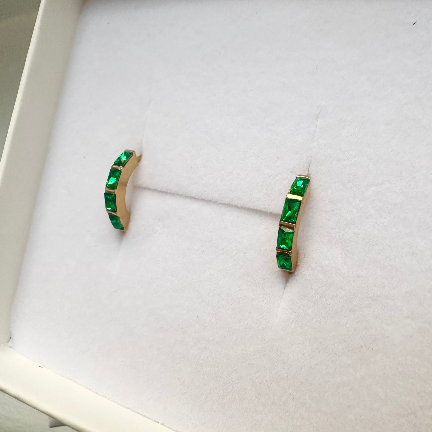 Pair of green gemstone earrings on a white cushioned stand