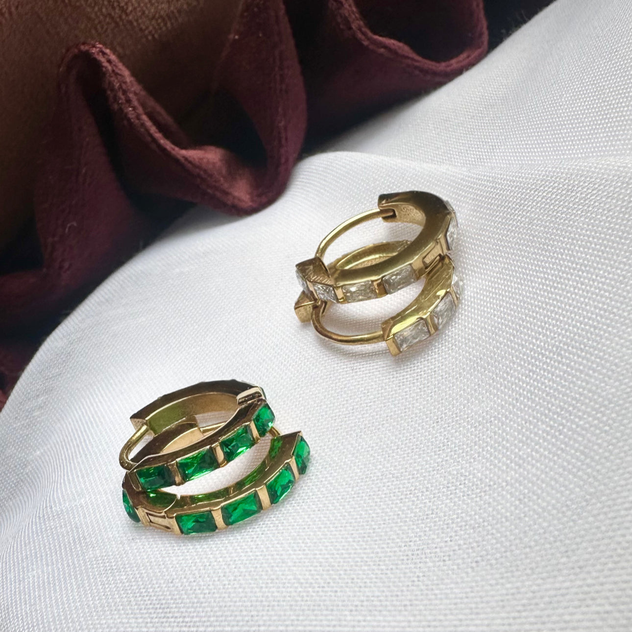 Gold hoop earrings with green gemstones on a white surface