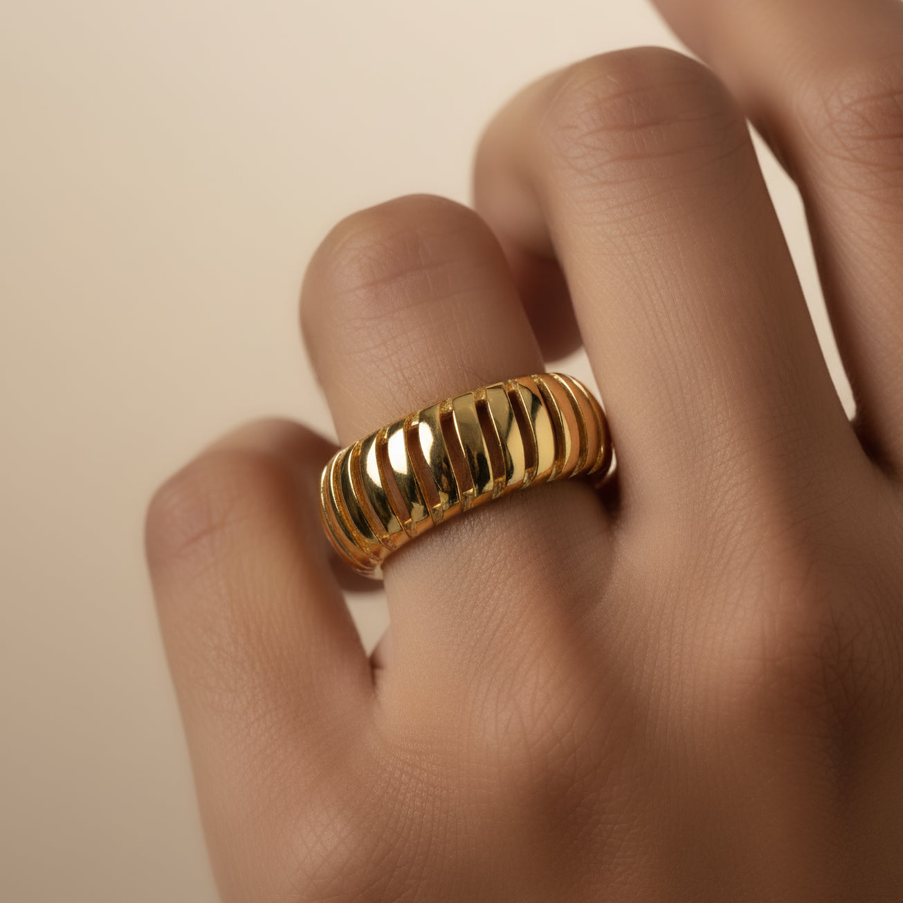 Gold ring on a finger against a beige background