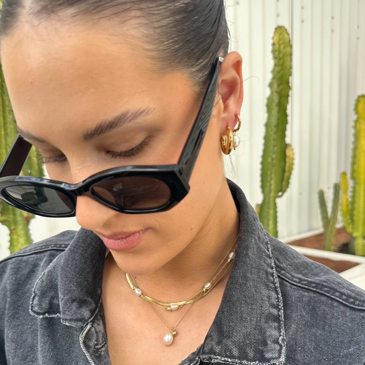 Woman wearing EVER Jewellery After Dark Pearl Hoop Earrings with Hustle Hoops, styled with layered pearl and gold necklaces, black sunglasses, and a denim jacket, with cacti in the background.