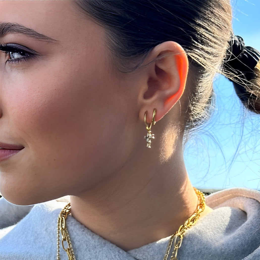 Close-up of woman wearing EVER Crossbar Dangle Huggies and layered gold chains