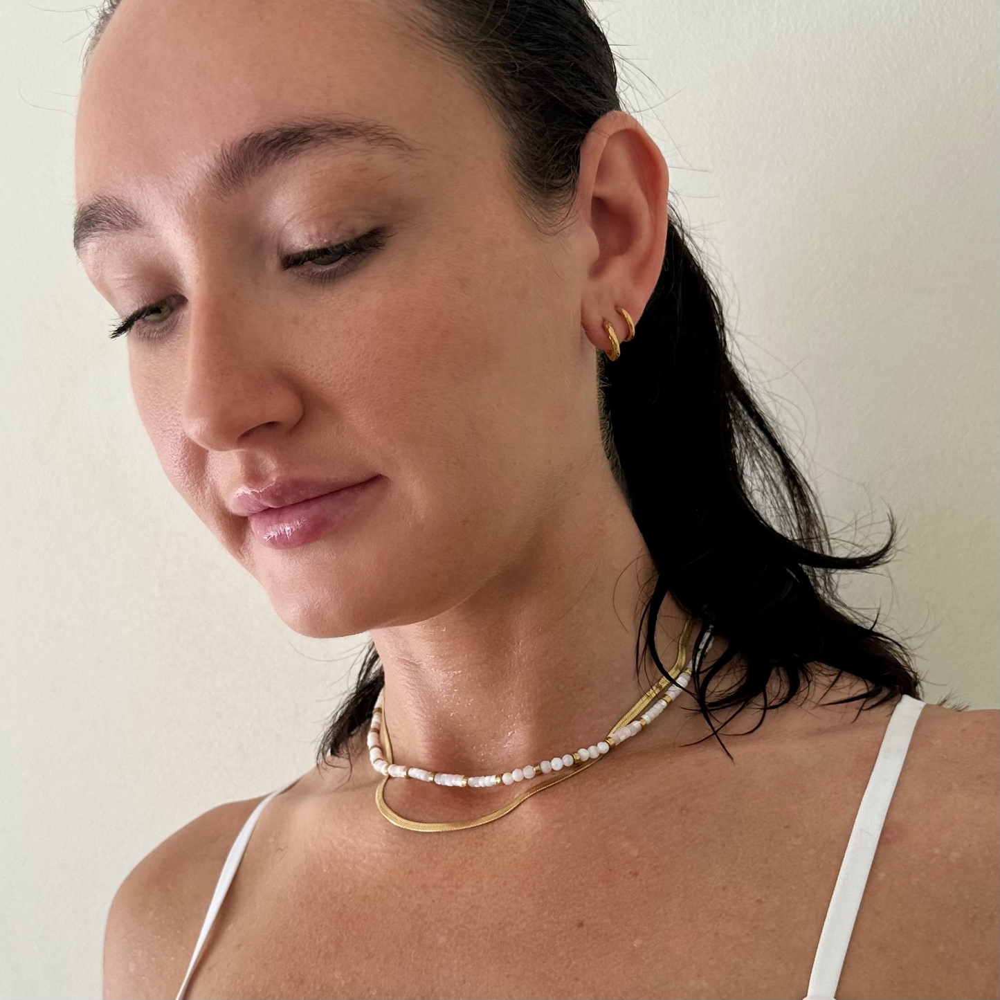 Woman wearing EVER Jewellery sweat proof Horizon Necklace with white beads and gold curved bar, styled with goSidewalk Necklace during work out.