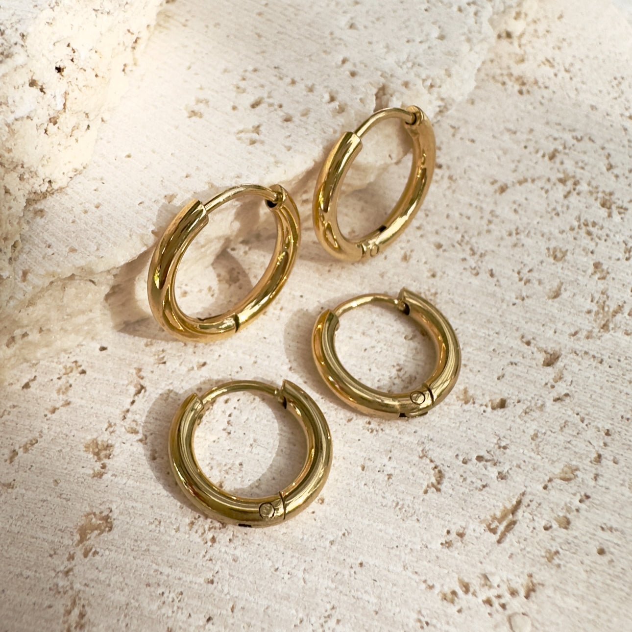 Flat lay of EVER Metro Sleeper Hoops in gold on textured stone