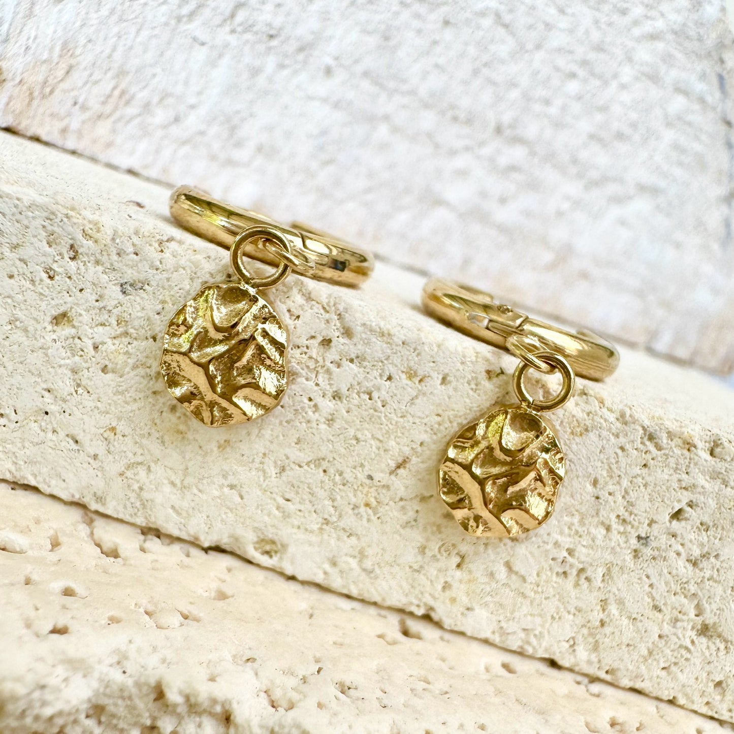 Flat lay of Harmony Gold Huggie Drop Earrings on neutral stone – durable waterproof gold earrings.