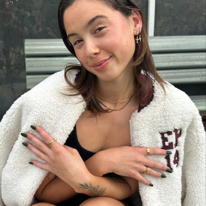 Woman wearing a white fleece jacket with text, sitting outdoors.
