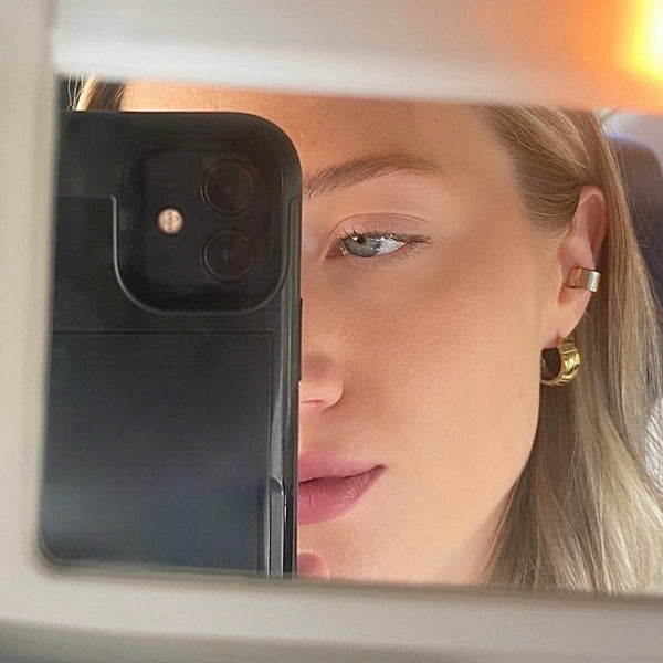 Woman looking into a car mirror with a phone case on the mirror