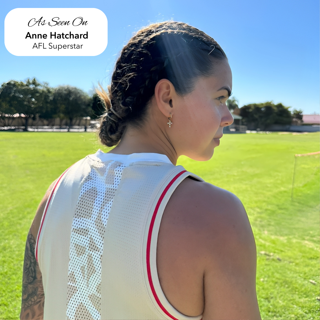 AFLW star Anne Hatchard on a sports field wearing EVER's gold cross huggie earrings, with braided hair and a white training singlet in full sun.