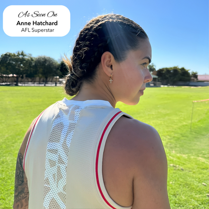 AFLW star Anne Hatchard on a sports field wearing EVER's gold cross huggie earrings, with braided hair and a white training singlet in full sun.