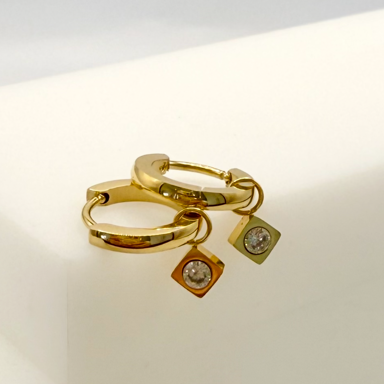 Gold hoop earrings with square pendants on a light background