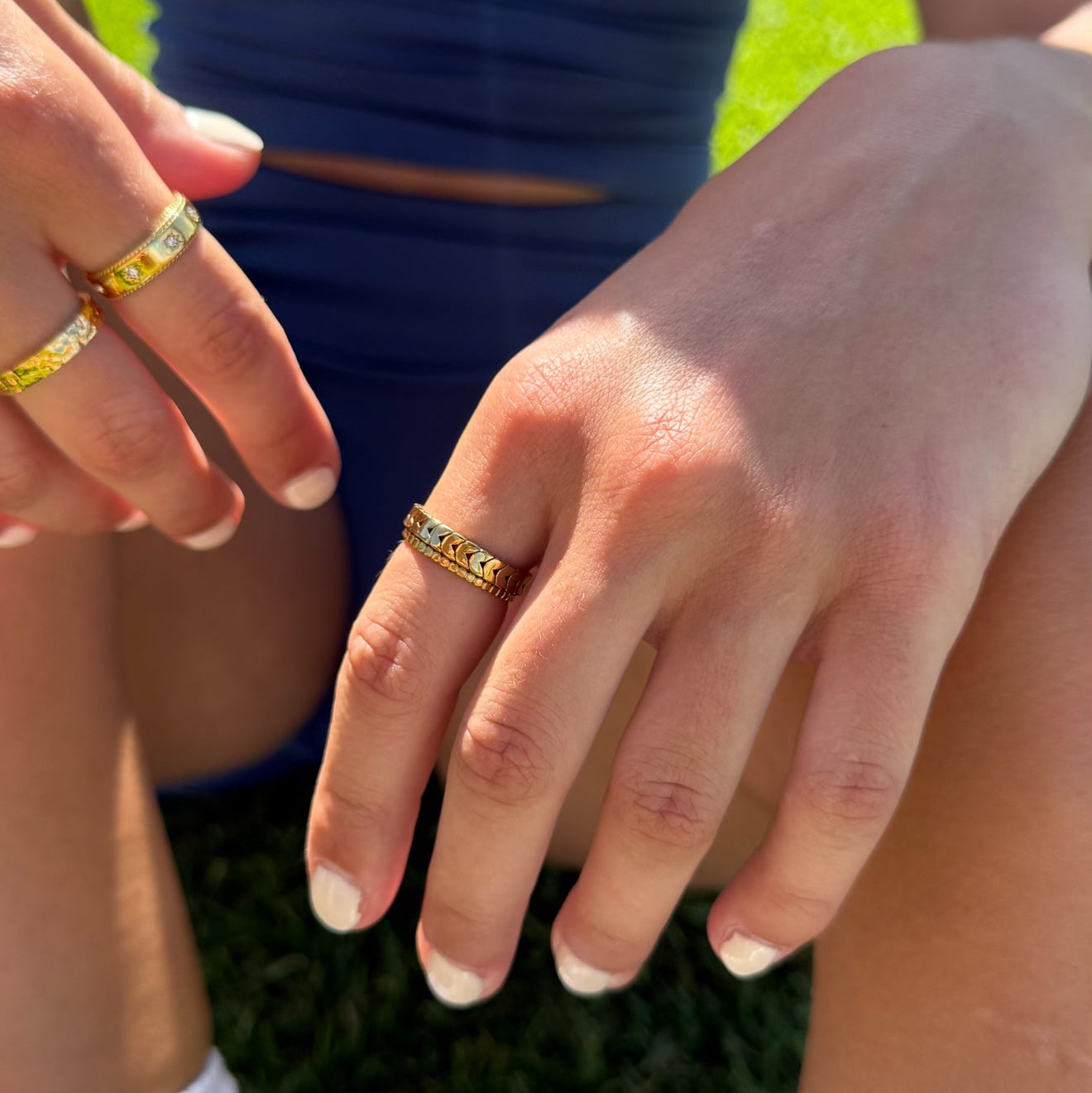 Close-up of two hands wearing gold rings with gemstones on a grassy background