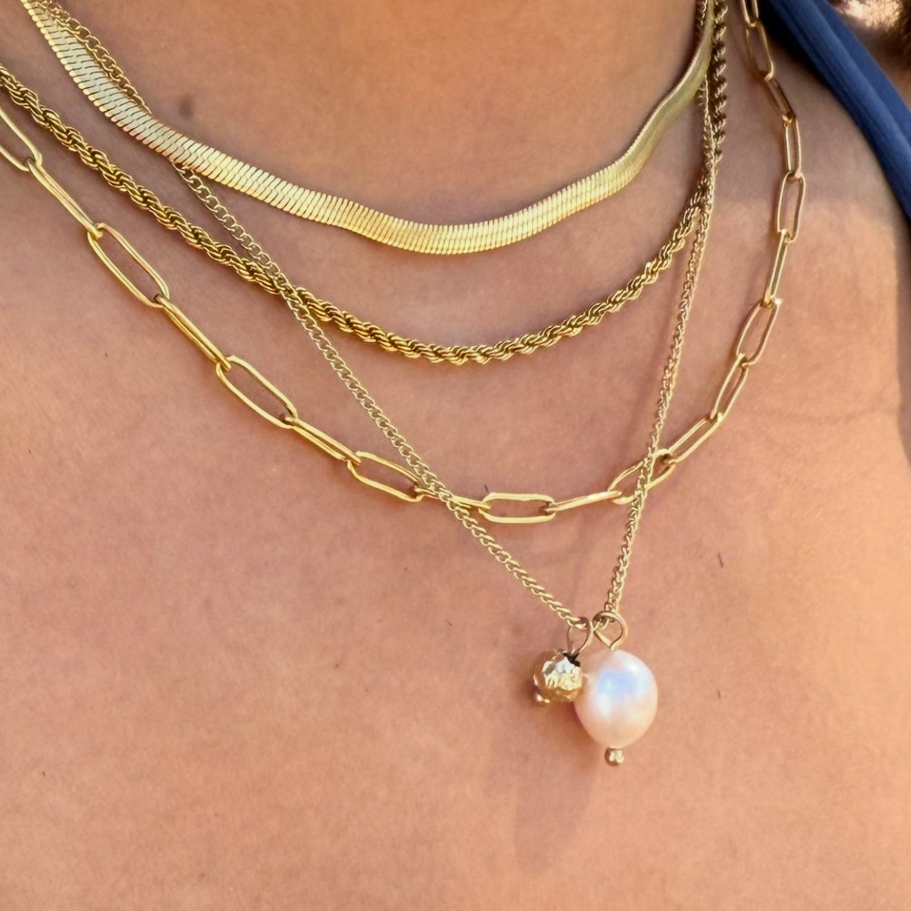 Close-up of a person wearing multiple gold necklaces with a pearl pendant.