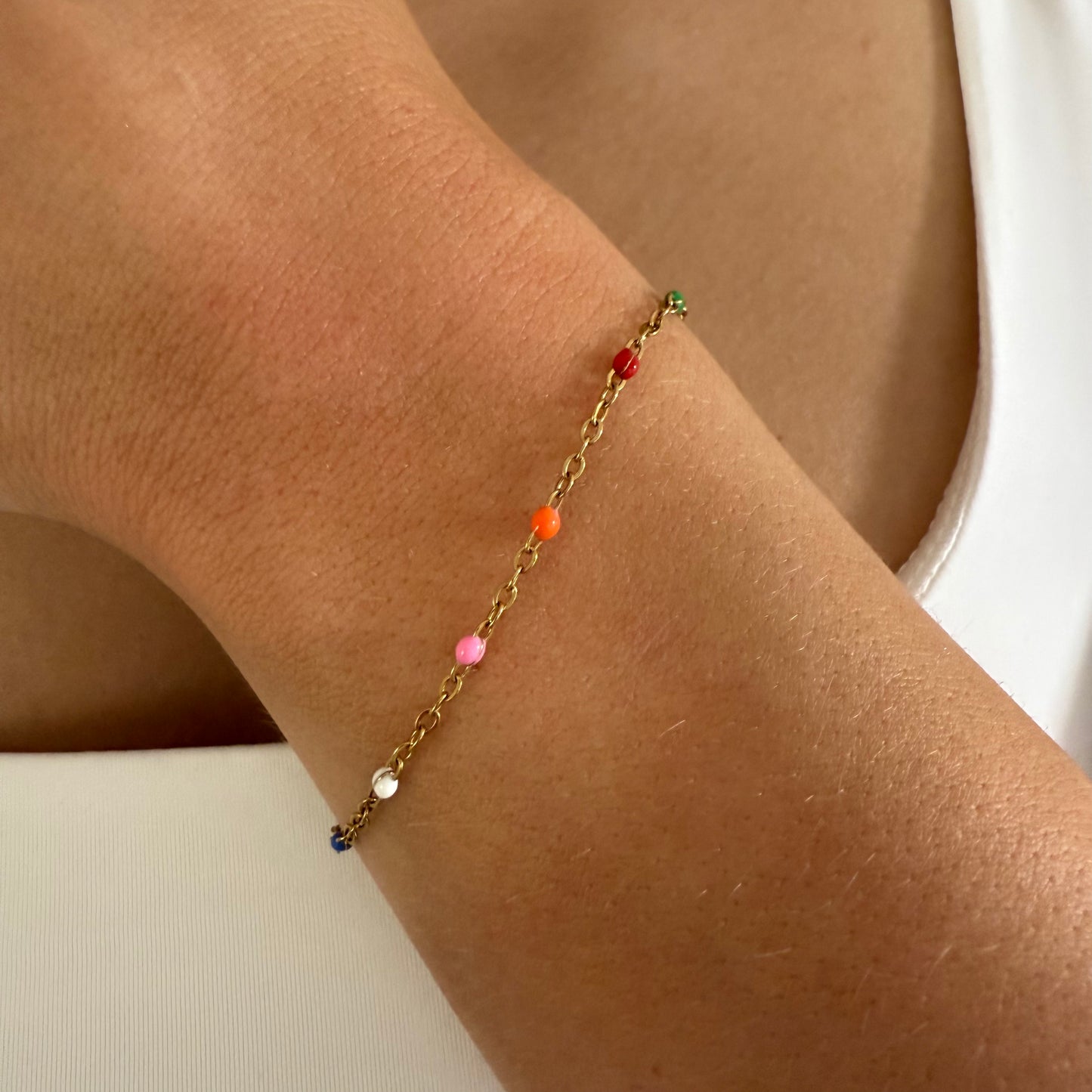 Gold bracelet with colorful beads on a wrist against a neutral background