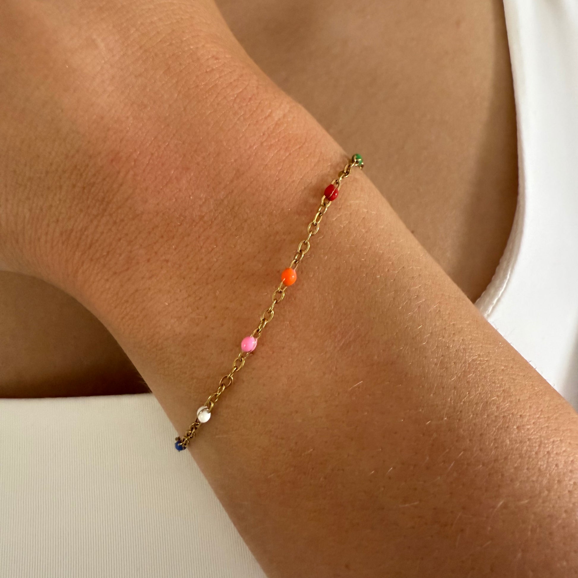 Gold bracelet with colorful beads on a wrist against a neutral background
