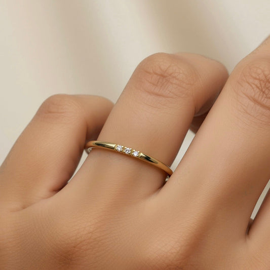 Gold ring with small diamonds on a finger against a neutral background